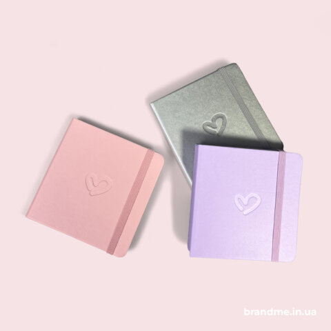 Рожевий, срібний та бузковий блокноти з тисненням у вигляді серця на обкладинці