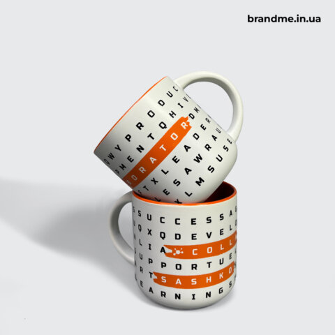 Дві білі чашки з чорним текстовим принтом та помаранчевими виділеннями слів