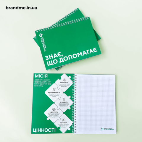 Зелений блокнот мережі аптек Подорожник з написом «Знає, що допомагає» та сторінками в клітинку